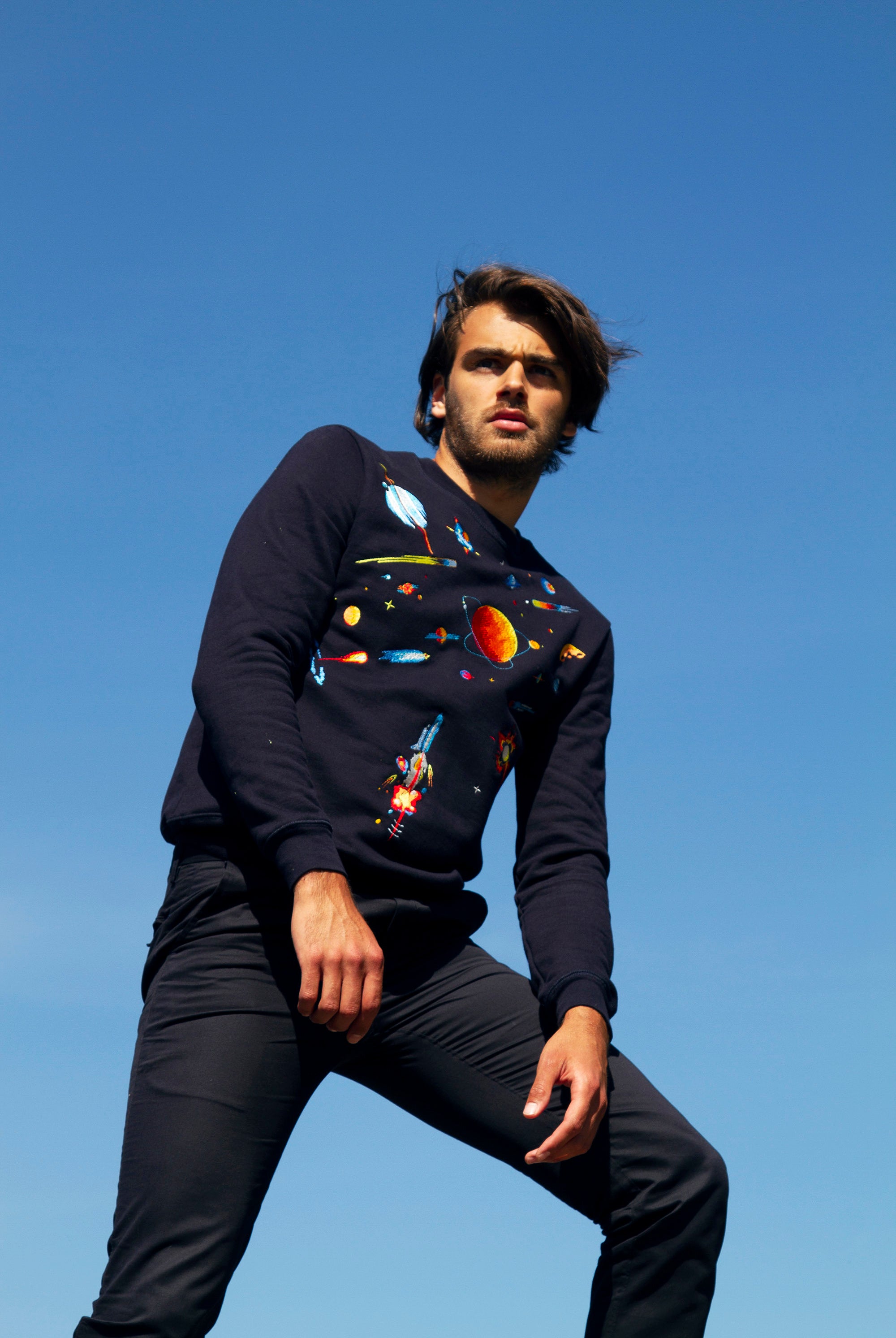 Homme brun debout contre-plongé regarde vers l'avenir sweat brodé cosmique fusée