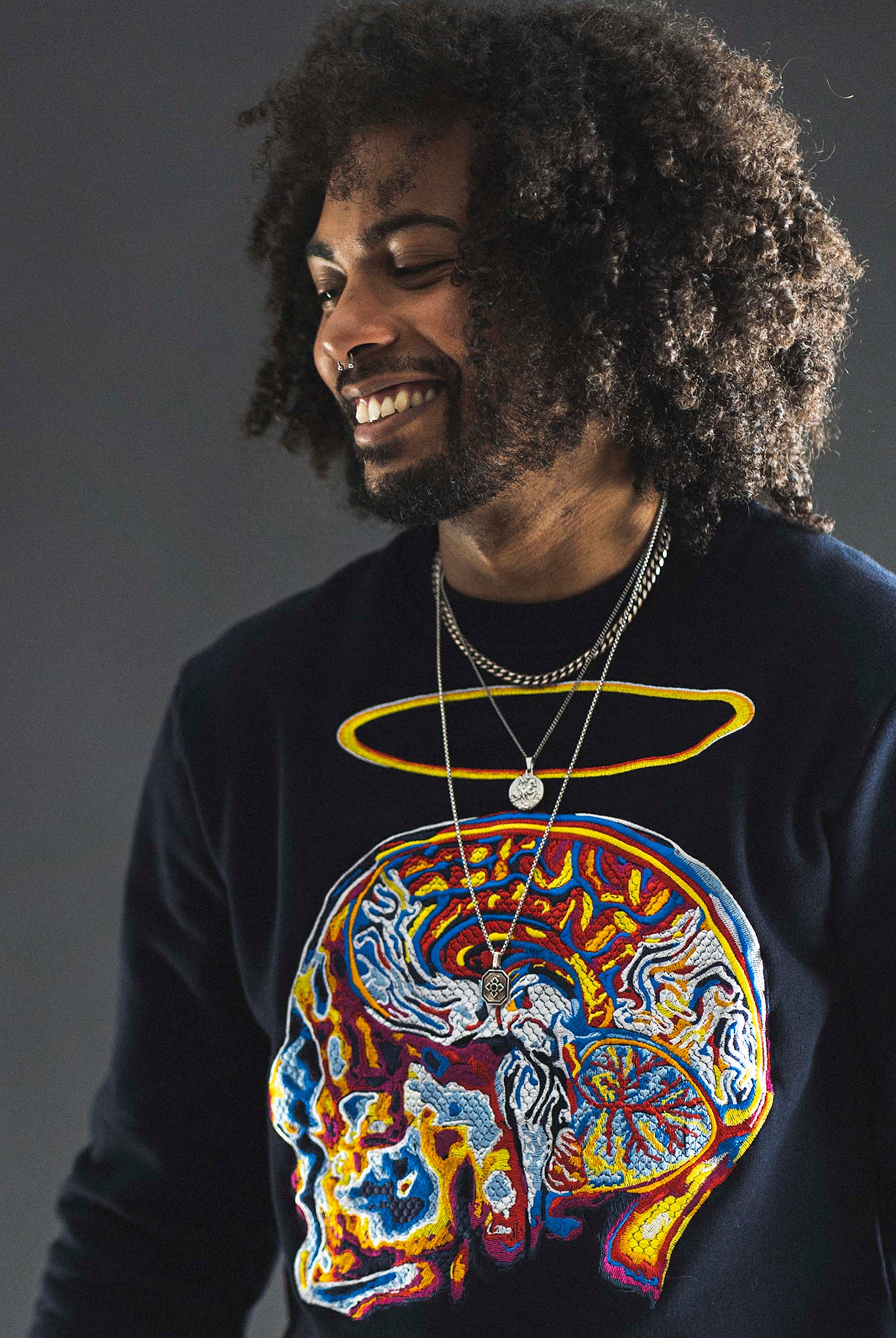 Jeune homme métisse souriant coupe afro sweat brodé crâne humain spirituel