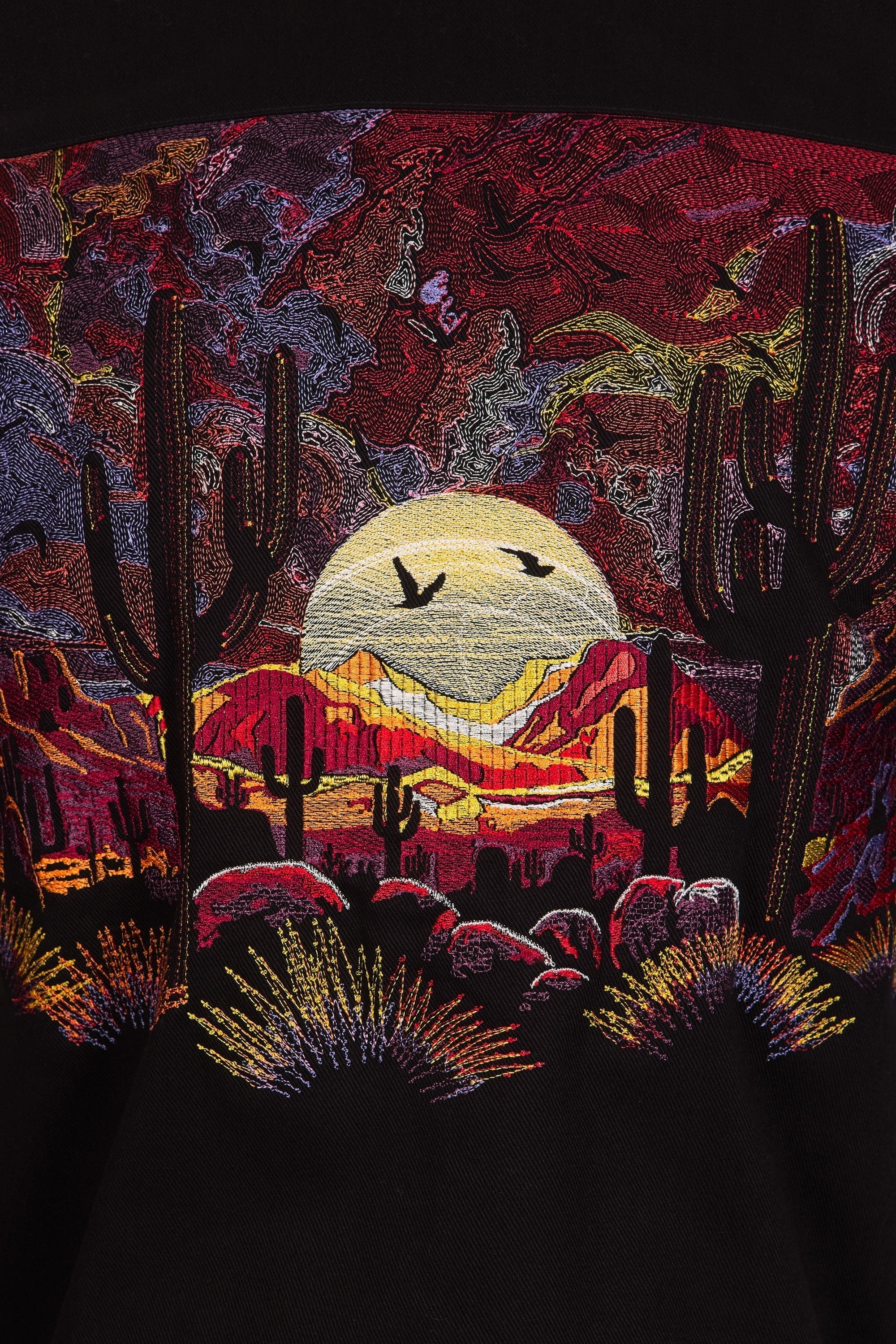 Broderie d'un paysage désertique aride, ou l'on peut voir des cactus et des montagnes ainsi qu'un coucher de soleil.