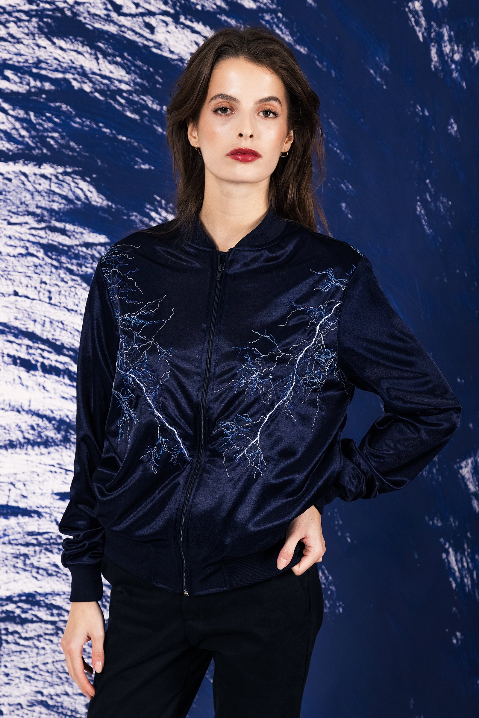 Jeune femme Brune se tenant debout avec une veste satinée type bomber brodé avec des éclairs 