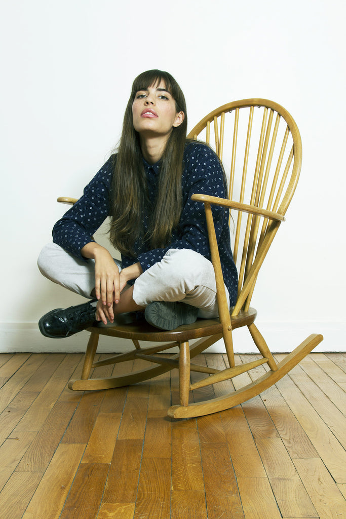 Jeune parisienne assise en tailleur sur un fauteuil en rotin