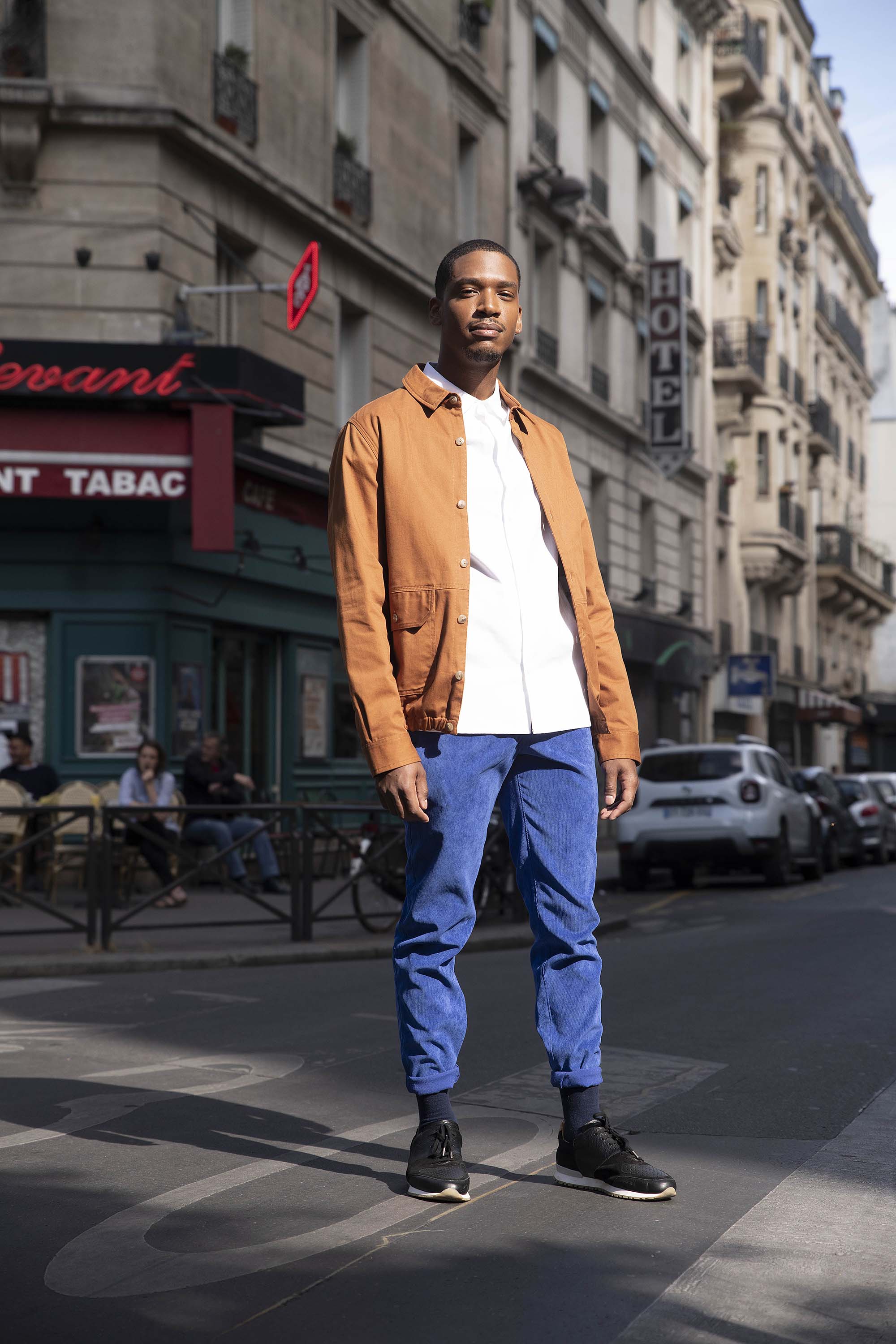 Jeune homme se tenant fièrement debout au milieu des rues parisiennes, commerces de proximité et shopping local
