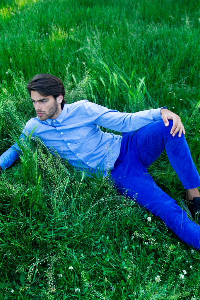 Homme allongé dans l'herbe regarde vers l'avenir, portant une chemise bleu ciel en coton pima qualité exceptionnelle