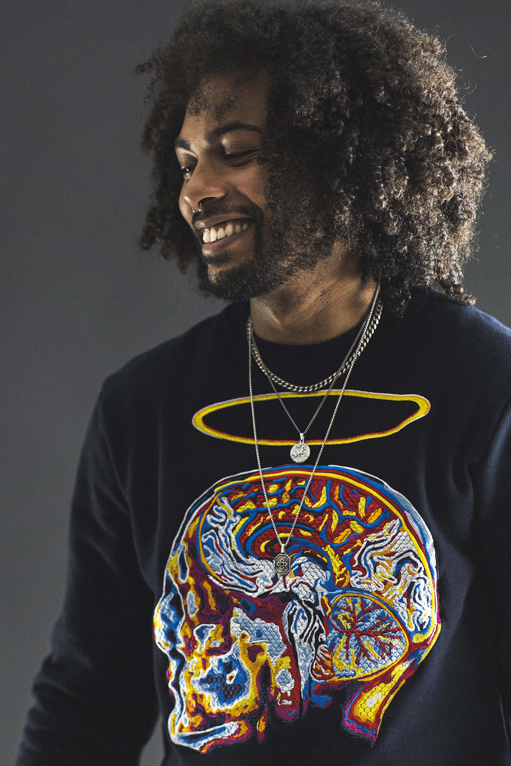 Jeune homme métisse souriant coupe afro sweat brodé crâne humain spirituel